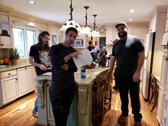 Three crew members reading script pages at a kitchen island, camera rig behind them