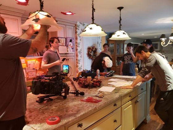 Camera rig on the kitchen counter while the crew sets up under pendant lamps