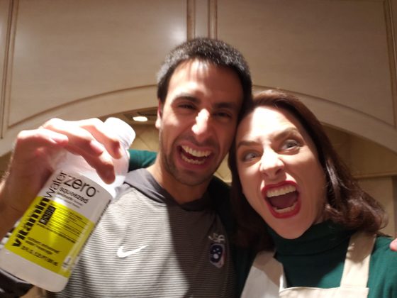 Two actors mugging for a close-up selfie, the kitchen set behind them