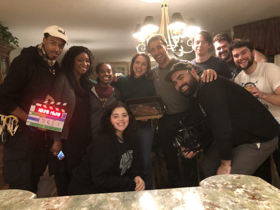 Cast and crew crowded around the dining table for a group photo with a clapperboard