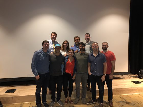 Cast and crew on the stage in front of the blank screen, arms around each other