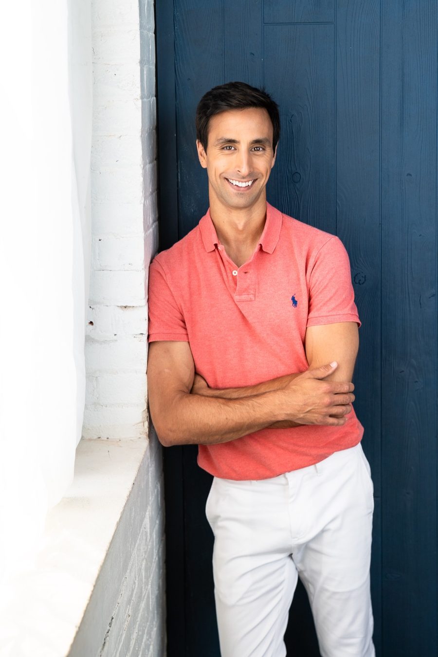 Tommy Hallal smiling with arms crossed, leaning against a blue door